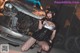 A woman in a black corset and fishnet stockings posing in front of a car.