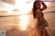 A woman in a floral dress standing on the beach at sunset.