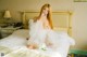 A woman in a white dress sitting on a bed.