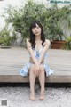 A woman sitting on a wooden bench in a blue and white dress.